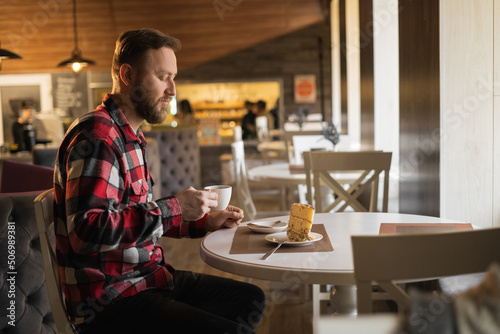 side view of young man having cup of coffee and eating pastry in a cafe