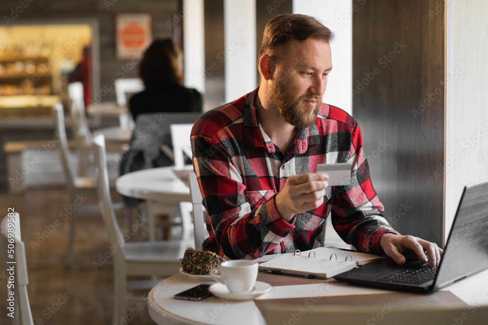handsome businessman shopping online with credit card using laptop in cafe, young man sitting in cafe while using laptop computer and debit card. handsome businessman shopping online with credit card using laptop in cafe, young man sitting in cafe while using laptop computer and debit card.
