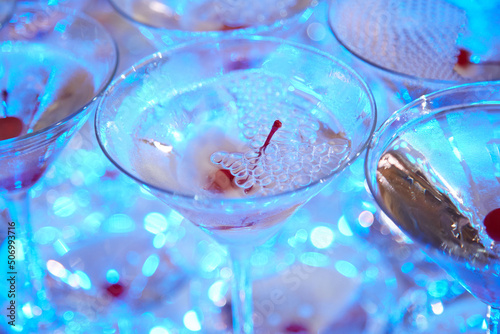 Cocktail glasses at an event or party. The glasses are on the buffet table. There is an alcoholic drink in the glasses  there is a cherry in the champagne glass
