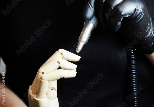 Manicure in the salon, wooden doll hand with a manicure and pedicure tool in the salon. Black background. Manicure and pedicure master in black gloves, hands. Hand care procedure photo