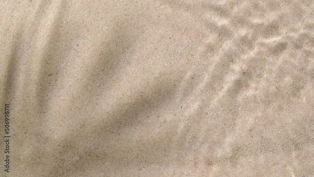 Slow motion water surface ripples and splash with palm tree leaf shadow on sand 