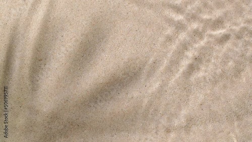 Slow motion water surface ripples and splash with palm tree leaf shadow on sand 