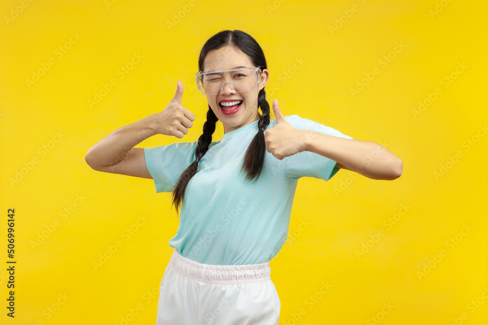 Happy Young Asian Woman showing thumb up over isolated yellow background, summer photo concept Happy Young Asian Woman showing thumb up over isolated yellow background, summer photo concept
