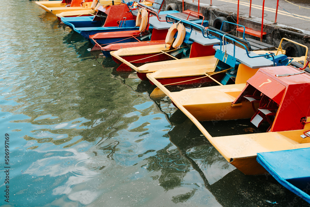 Close-up of a catamaran boat station in park on sunny day. Parked colorful catamarans on water. Active recreation, entertainment