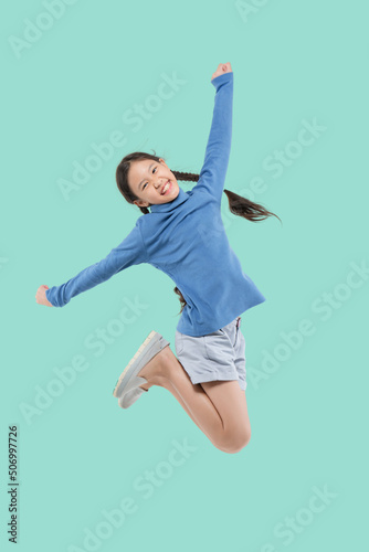 Happy little Asian child girl jumping isolated on pastel green background.