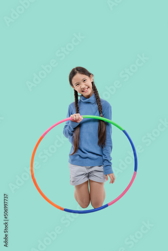Portrait of happy little Asian child girl playing hula hoop on isolated pastel green background © RedcupStudio
