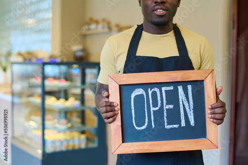 Close-up of african male owner holding blackboard with open sign in his hands, he opening his new coffee shop
