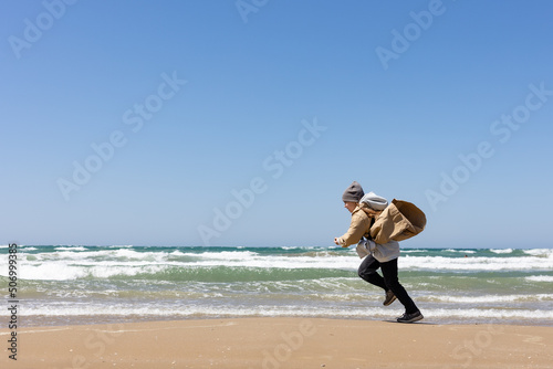 a six-year-old girl in a beige trench coat runs along the sandy seashore in windy weather