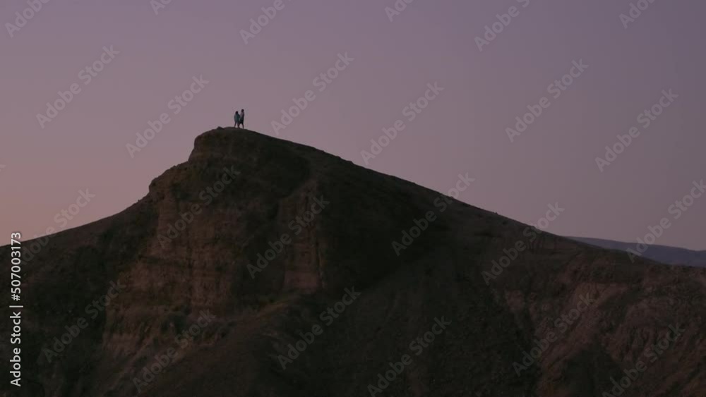 A couple standing on top of mountain at Zabriskie Point at Death Valley National Park, enjoying the sunset and blue hour. A couple standing on top of mountain at Zabriskie Point at Death Valley National Park, enjoying the sunset and blue hour.