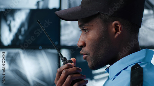 Fotografia Close up of security guard look at monitor and report on walkie talkie