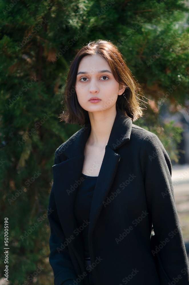 A beautiful young girl looks into the camera. The girl is walking on the street. Vertical photo. A beautiful young girl looks into the camera. The girl is walking on the street. Vertical photo.