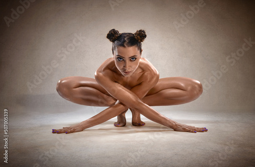 Beautiful nude sexy fitness girl with great figure flexing her perfect body in a yoga pose.