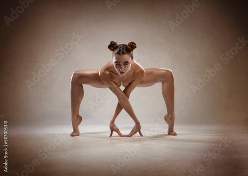 Beautiful nude sexy fitness girl with great figure flexing her perfect body in a yoga pose