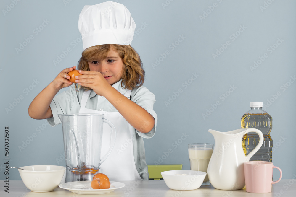 Kid boy in chef hat and apron cooking preparing meal. Little cook with vegetables at kitchen. Natural kids food. Kid boy in chef hat and apron cooking preparing meal. Little cook with vegetables at kitchen. Natural kids food.