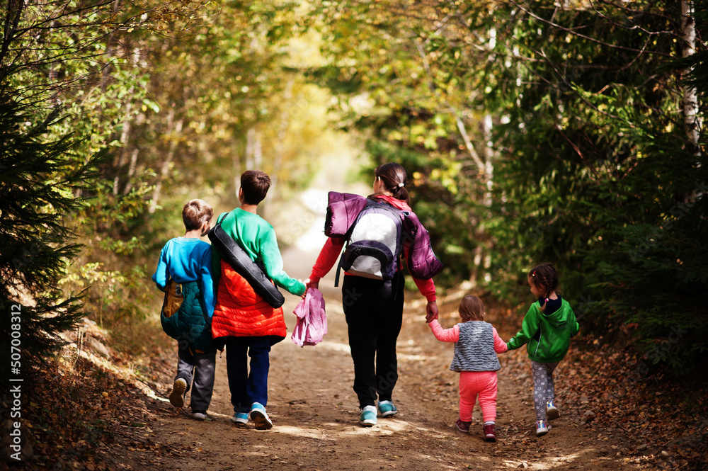 Back of mother with four kids walking on wood mountains. Family travel and hiking with childrens. Wear backpack. Back of mother with four kids walking on wood mountains. Family travel and hiking with childrens. Wear backpack.