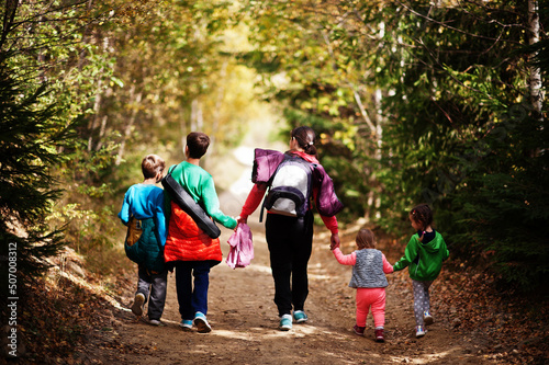 Back of mother with four kids walking on wood mountains. Family travel and hiking with childrens. Wear backpack.