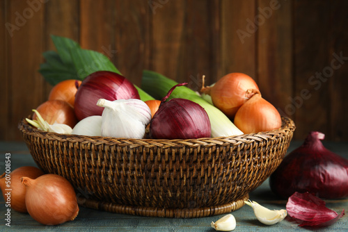 Wicker basket with fresh onion bulbs  leeks and garlic on light blue wooden table