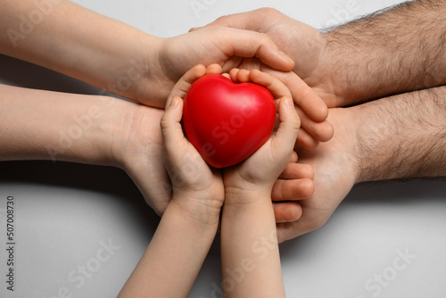Parents and kid holding red heart in hands on light grey background, top view