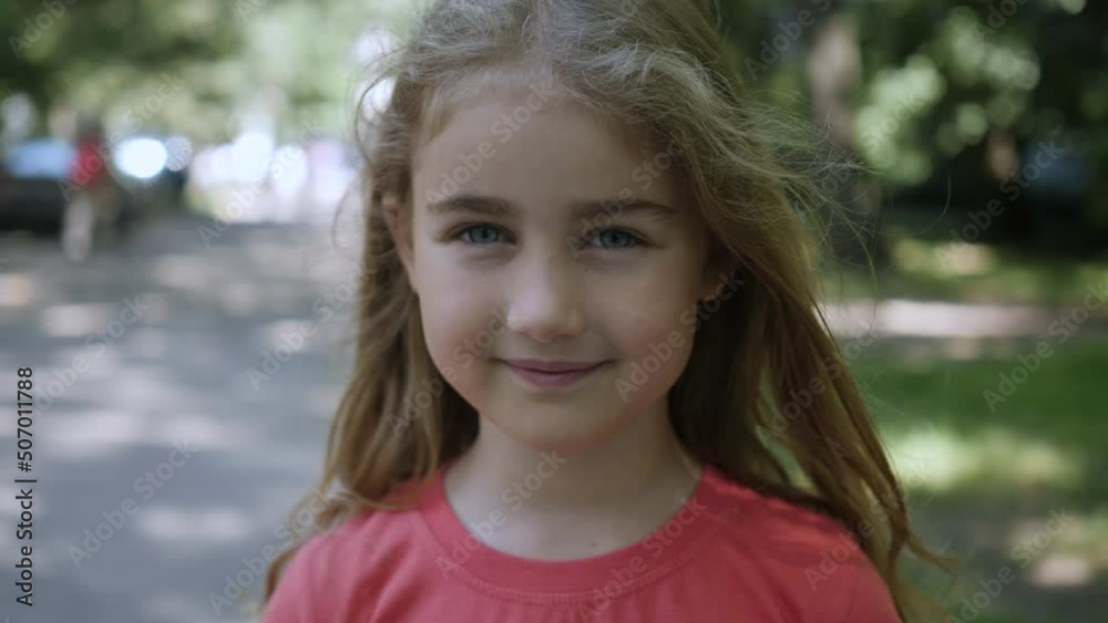 Young Happy Thinking Curiosity Child Looking at Camera Closeup Outdoors. Face Eyes Serious Contemplative Child. Portrait Little Child Girl Looking at Camera Standing on Street in City on Summer Day. Young Happy Thinking Curiosity Child Looking at Camera Closeup Outdoors. Face Eyes Serious Contemplative Child. Portrait Little Child Girl Looking at Camera Standing on Street in City on Summer Day.