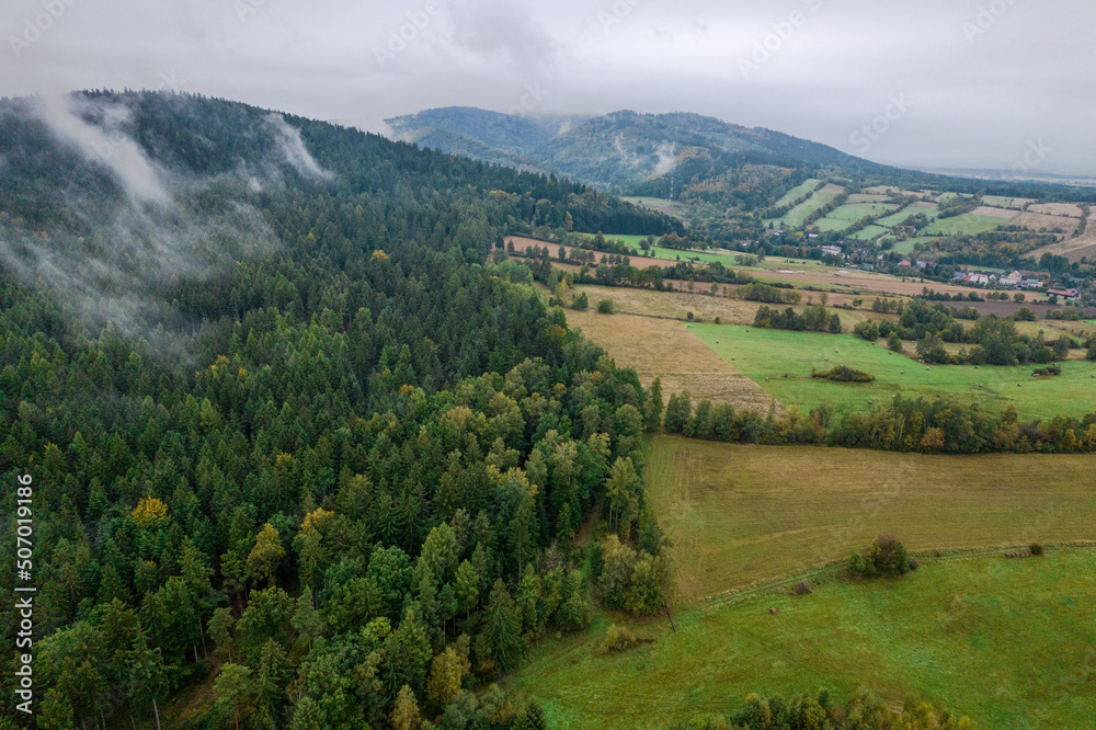 Obraz premium Aerial view of the foggy morning at the forest and green hills. 