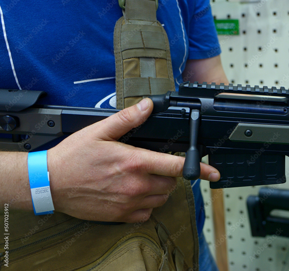 Man hands holding a new model of a rifle in a gun shop, rifles on a stand