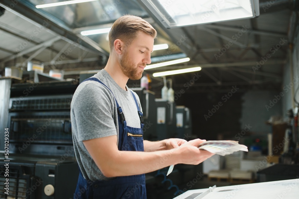 Portrait of production line worker controlling manufacturing process of modern packaging industrial machine in printing factory Portrait of production line worker controlling manufacturing process of modern packaging industrial machine in printing factory