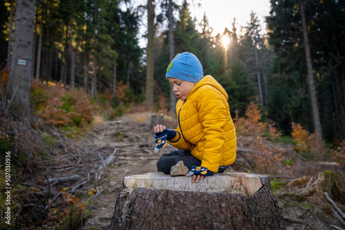 Little kid is sitting on a big stump on the mountain trail, eating. Fall season