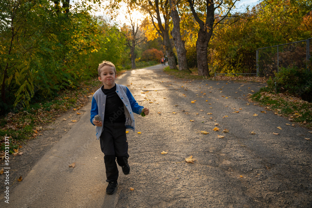 Fototapeta premium The little kid is running along the asphalt road after the hike is over. Fall season