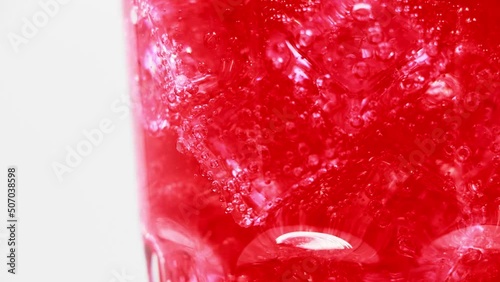 Red sparkling water with Ice in glass over white background. Rotate glass of Red sparkling water drink over white background.