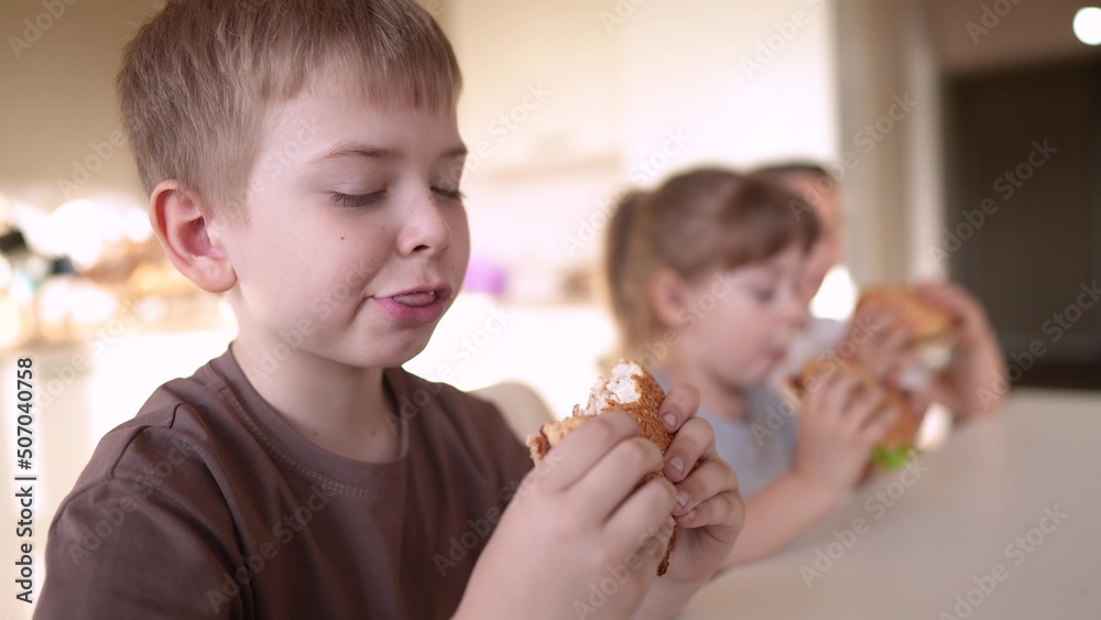 children eat burgers. fast food burger. a group of small children in the kitchen greedily eat fast food burgers. big family small fun kids having breakfast in the morning in the kitchen eating burger children eat burgers. fast food burger. a group of small children in the kitchen greedily eat fast food burgers. big family small fun kids having breakfast in the morning in the kitchen eating burger