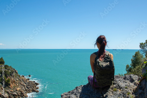 Woman trekker sits on the top of the mountain above the sea