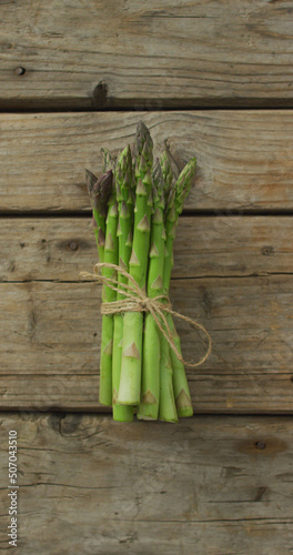 Vertical image of fresh stalks of asparagus tied with rustic string on rustic background
