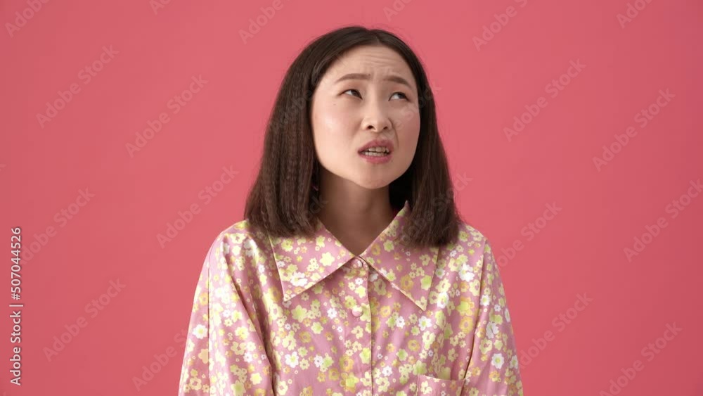 Displeased Asian woman thinking and looking around in the pink studio Displeased Asian woman thinking and looking around in the pink studio