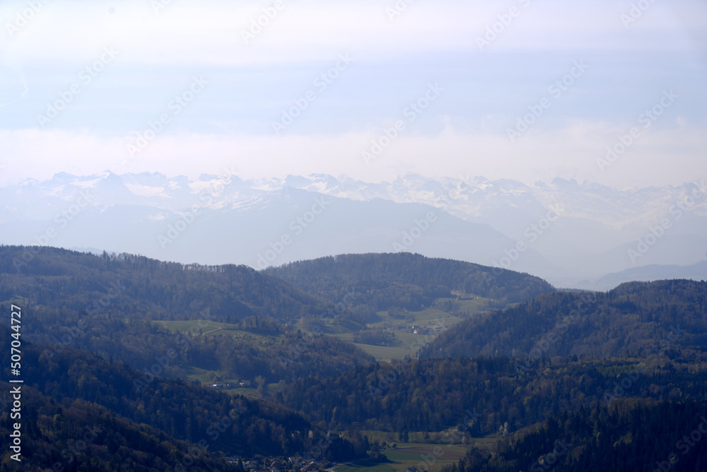 Aerial view over rural landscape with Swiss Alps in the background seen from local mountain Uetliberg on a blue cloudy spring day. Photo taken April 21st, 2022, Zurich, Switzerland.