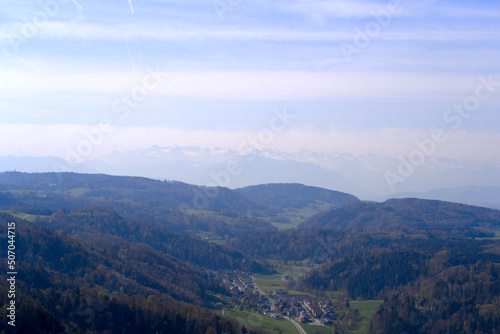 Aerial view over rural landscape with Swiss Alps in the background seen from local mountain Uetliberg on a blue cloudy spring day. Photo taken April 21st, 2022, Zurich, Switzerland.
