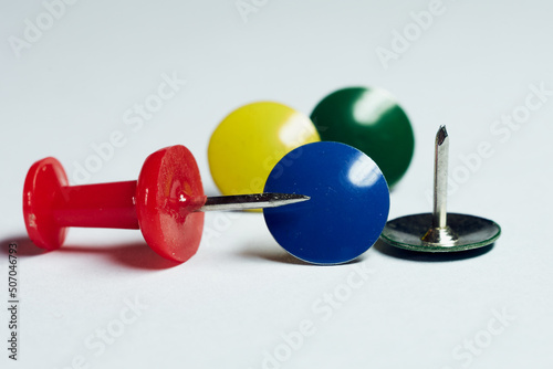 Multi-colored buttons for fixing notes or paper lie on a white background, a simple still life of office supplies, an abstract idea, a closeup © Dmitrii