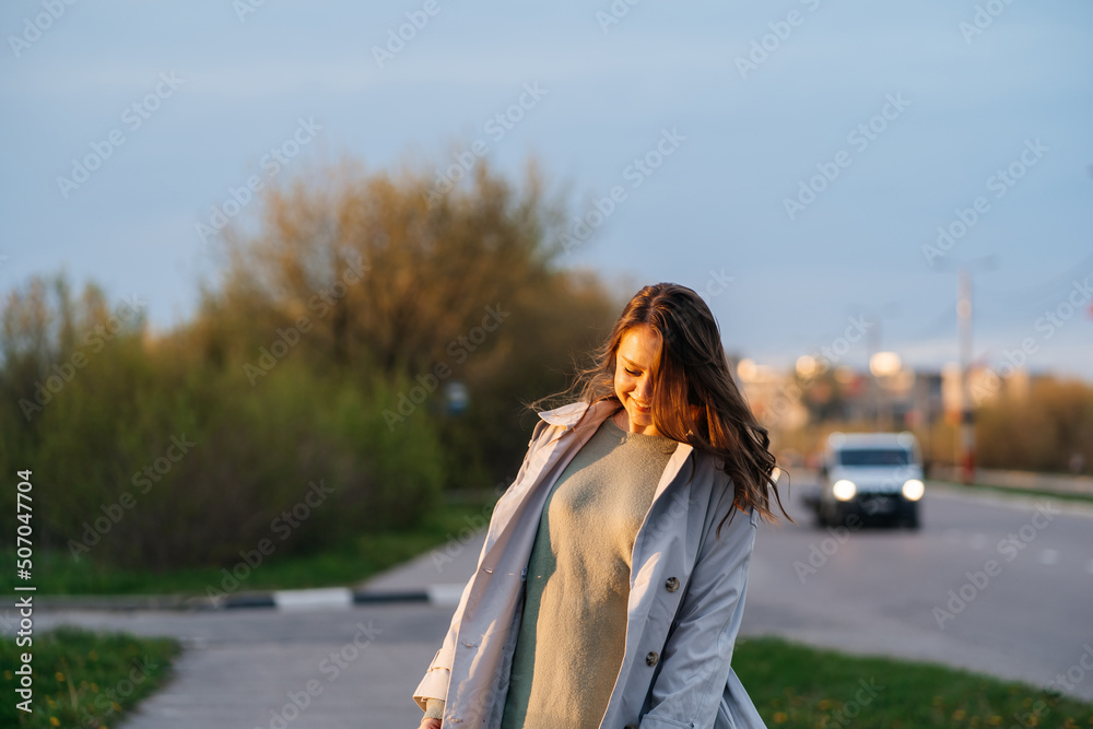 beautiful smiling girl with long hair in a grey trench coat outdoors on the street spring beautiful smiling girl with long hair in a grey trench coat outdoors on the street spring