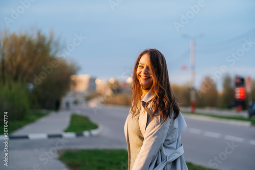 beautiful smiling girl with long hair in a grey trench coat outdoors on the street spring