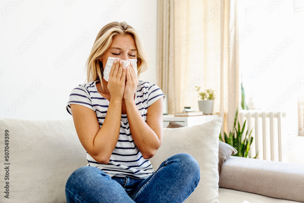 Shot of an attractive young woman suffering with the flu while sitting on her bed at home. The sick woman, holding a handkerchief, sneezing and feeling freezing, sitting on bed at home. Health problem Shot of an attractive young woman suffering with the flu while sitting on her bed at home. The sick woman, holding a handkerchief, sneezing and feeling freezing, sitting on bed at home. Health problem