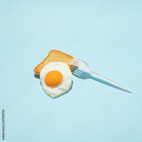 Fried egg on toast with white plastic fork. Minimal creative food concept. photo