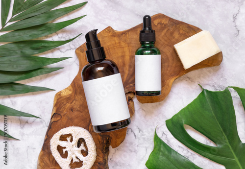 Natural cosmetics in glass bottles on a wooden board near tropical leaves, mockup, top view photo