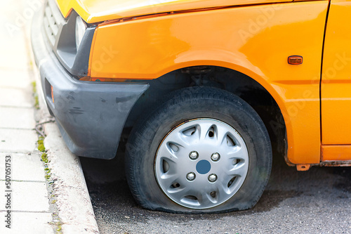 Punctured front wheel of an orange car on the road,, flat car tire close-up. Accident, emergency stop.Help on the road with a puncture. Tire service.
