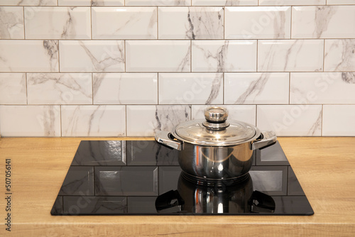 Cooking stainless still pan at modern kitchen induction cooker hob and wooden counter and white tile backsplash
