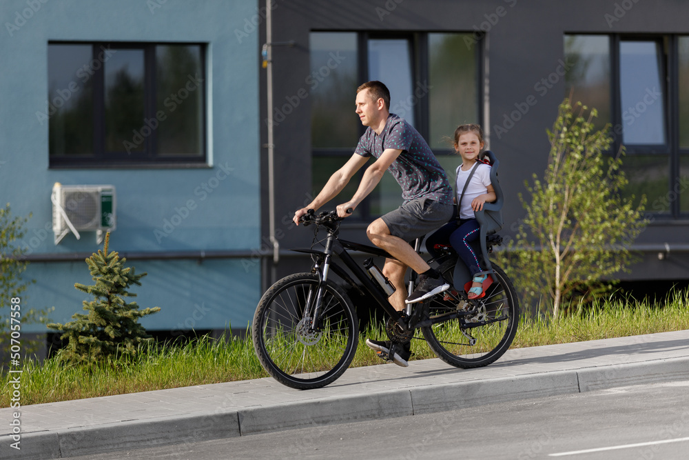 The father rides on a bicycle small daughter in a children's seat The father rides on a bicycle small daughter in a children's seat