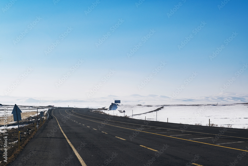 View of an emtpy road with yellow lanes and snow in winter