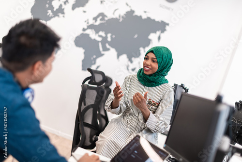 Multiethnic startup business team Arabian woman wearing a hijab on meeting in modern open plan office interior brainstorming, working on laptop and desktop computer. Selective focus 