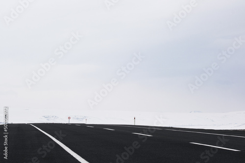 Diagonal view of an emtpy asphalt and bending road with lanes and snow in winter