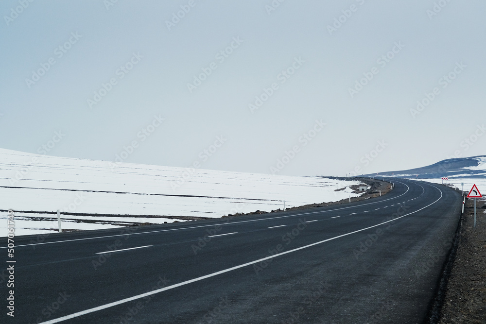 Fototapeta premium Diagonal view of an emtpy asphalt and bending road with lanes and snow in winter
