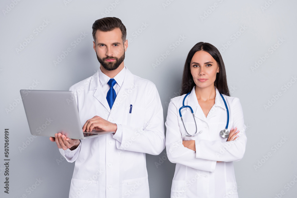 Photo of serious confident two doctors wear white coats online consultation modern device isolated grey color background Photo of serious confident two doctors wear white coats online consultation modern device isolated grey color background