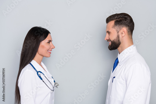 Photo of confident positive two doctors wear white coats looking each other isolated grey color background